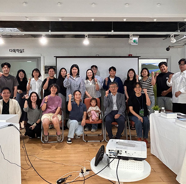 다목적실에서 한자리에 모인 남녀노소 참여자들이 정면을 향해 파이팅 포즈를 취하며 단체 기념사진을 촬영하고 있는 모습