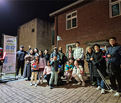 야간에 '나주읍성 플로깅' 배너 옆에서 아이들과 성인들이 함께 모여 야간 활동 준비를 마치고 밝게 웃으며 단체 사진을 찍는 모습