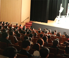 어두운 공연장 객석을 가득 채운 관객들이 밝게 빛나는 무대 위에서 펼쳐지는 공연이나 행사를 집중해서 관람하는 뒷모습